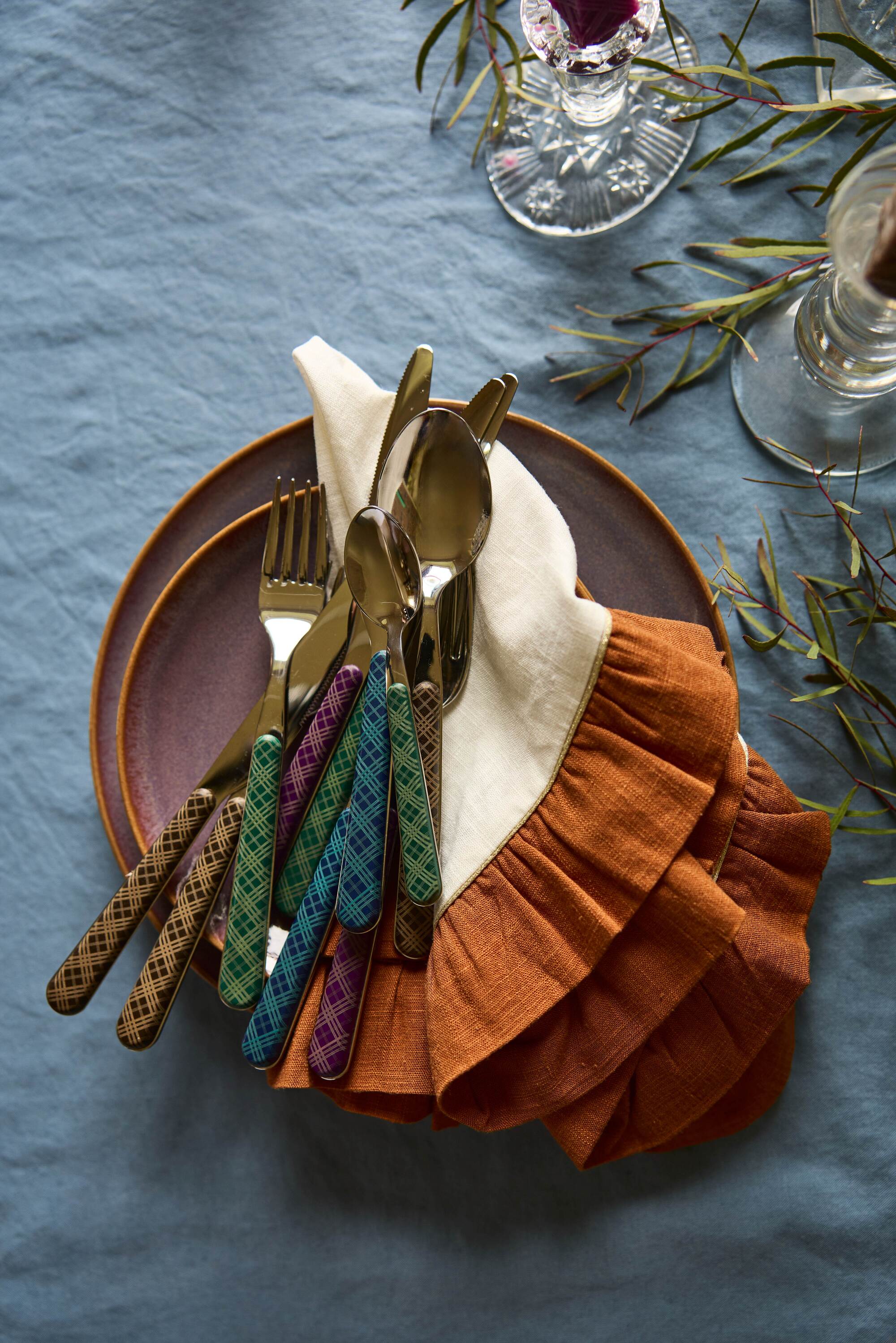 Image of tartan cutlery on a white and burnt orange napkin on a table that has a deep blue tablecloth.