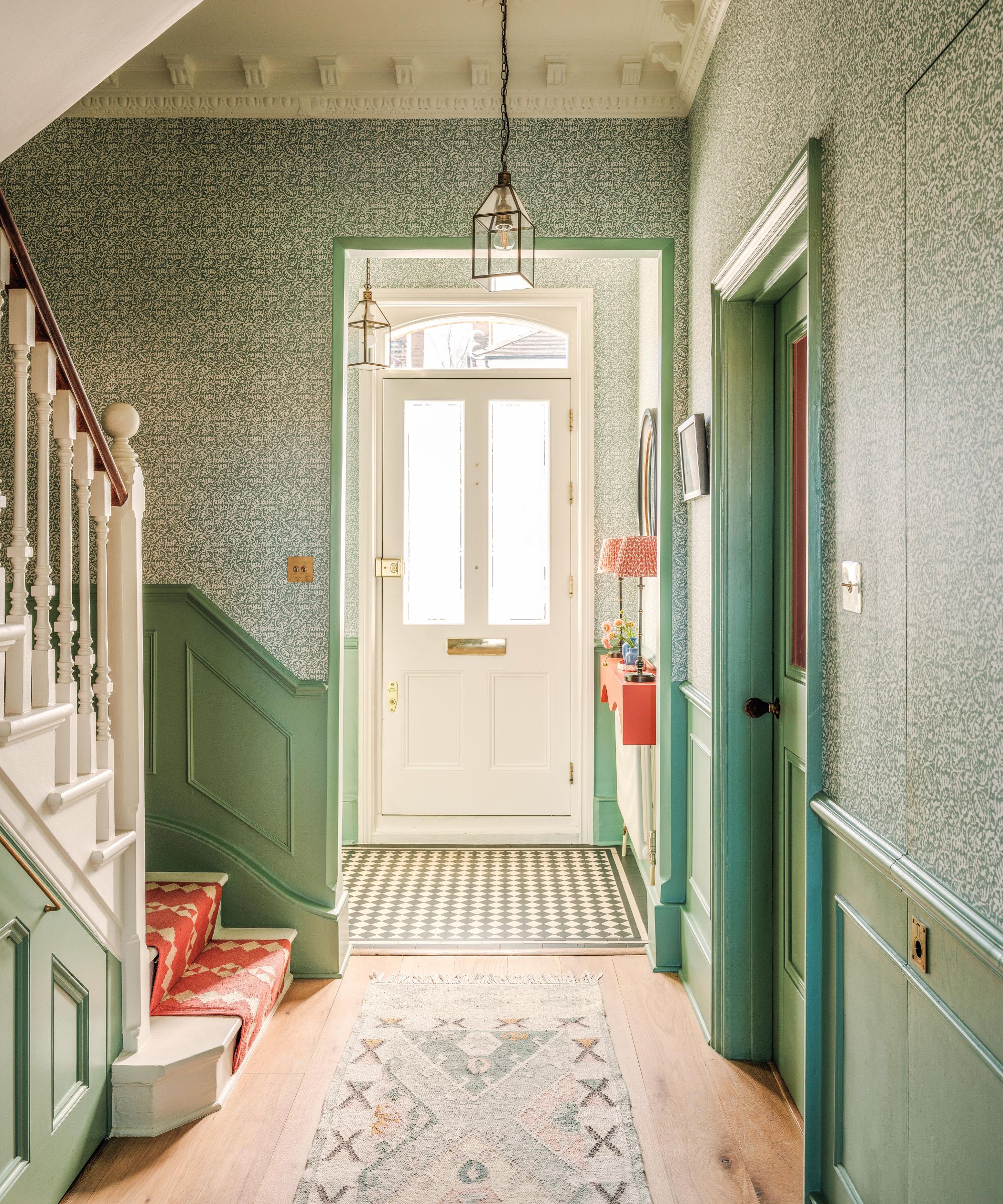 a grand Victorian entryway with a white painted staircase, red runner on the stairs, green wallpaper and paneling on the walls and a porch area with tiled floor