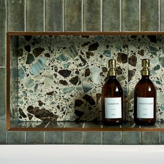 detail of a bath area with dark green tiles and a terrazzo recessed cubby shelf for toiletries