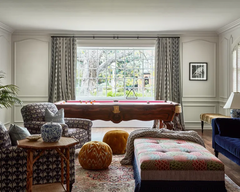 Light living room with rich colored upholstered couches and pool table in front of window with curtains