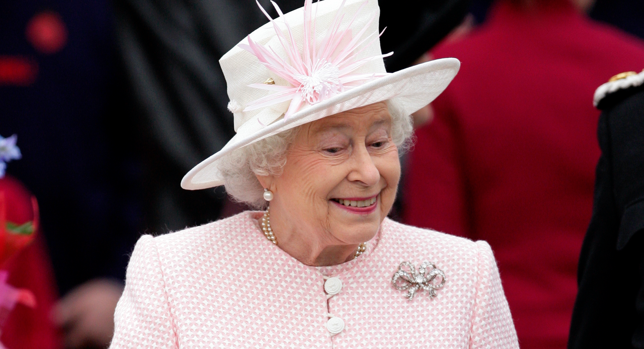 Queen Elizabeth wears a pink jacket featuring white buttons, and a white hat with pink detailing