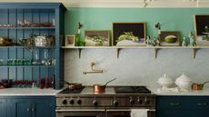 A kitchen with green walls, a marble countersplash, and a navy blue hutch decorated with kitchenware and decor