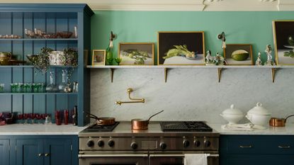 A kitchen with green walls, a marble countersplash, and a navy blue hutch decorated with kitchenware and decor