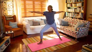 Woman doing yoga in her living room in the morning as sunshine comes through the curtains