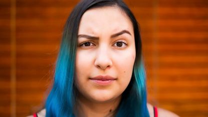 A young woman with blue hair raises her eyebrows in distrust.