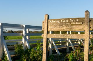 Wooden sign by a bridge under a clear blue sky in summer in the Wealden district. Also showing directions to Litlington, East Sussex, UK