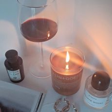 Best Autumn Candles: Malin & Goetz Tobacco candle burning alongside a glass of red wine and a bottle of Acqua di Parma perfume