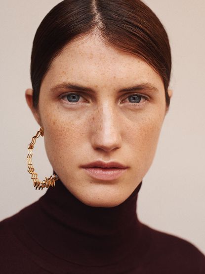 Model wearing one gold hoop earring 