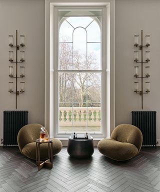 arched window with two green statement chairs and parquet floor with linear wall lights