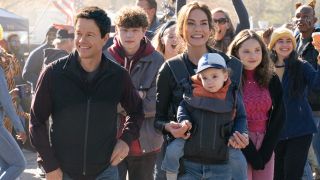 Van Crosby, Mark Wahlberg, Zoe Colletti, and Michelle Monaghan walking through a celebrating college campus in The Family Plan.