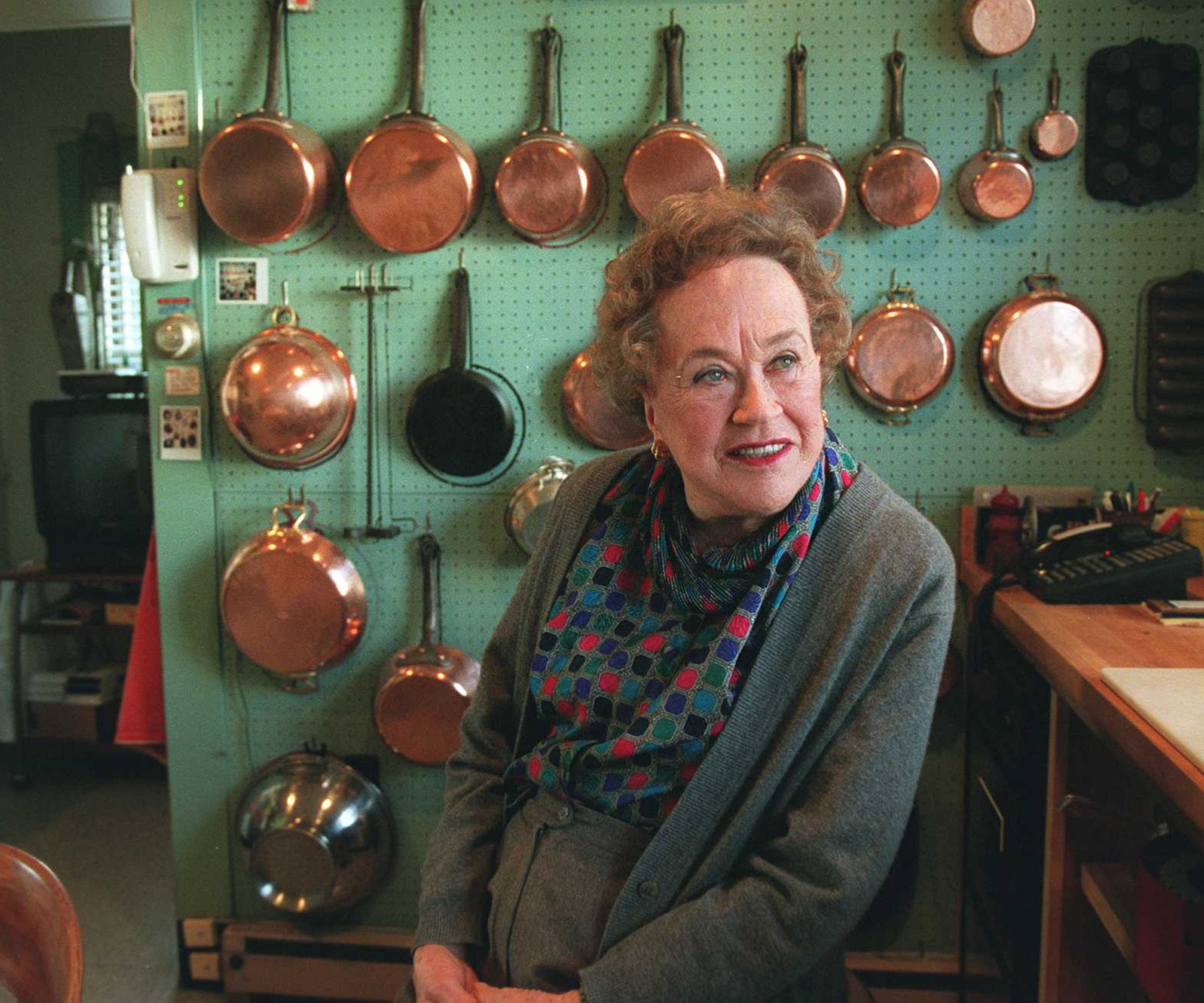 Julia Child in front of a turquoise wall of copper pans and pots