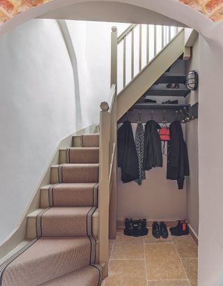 understairs boot room in hall with tiled floor, staircase with runner