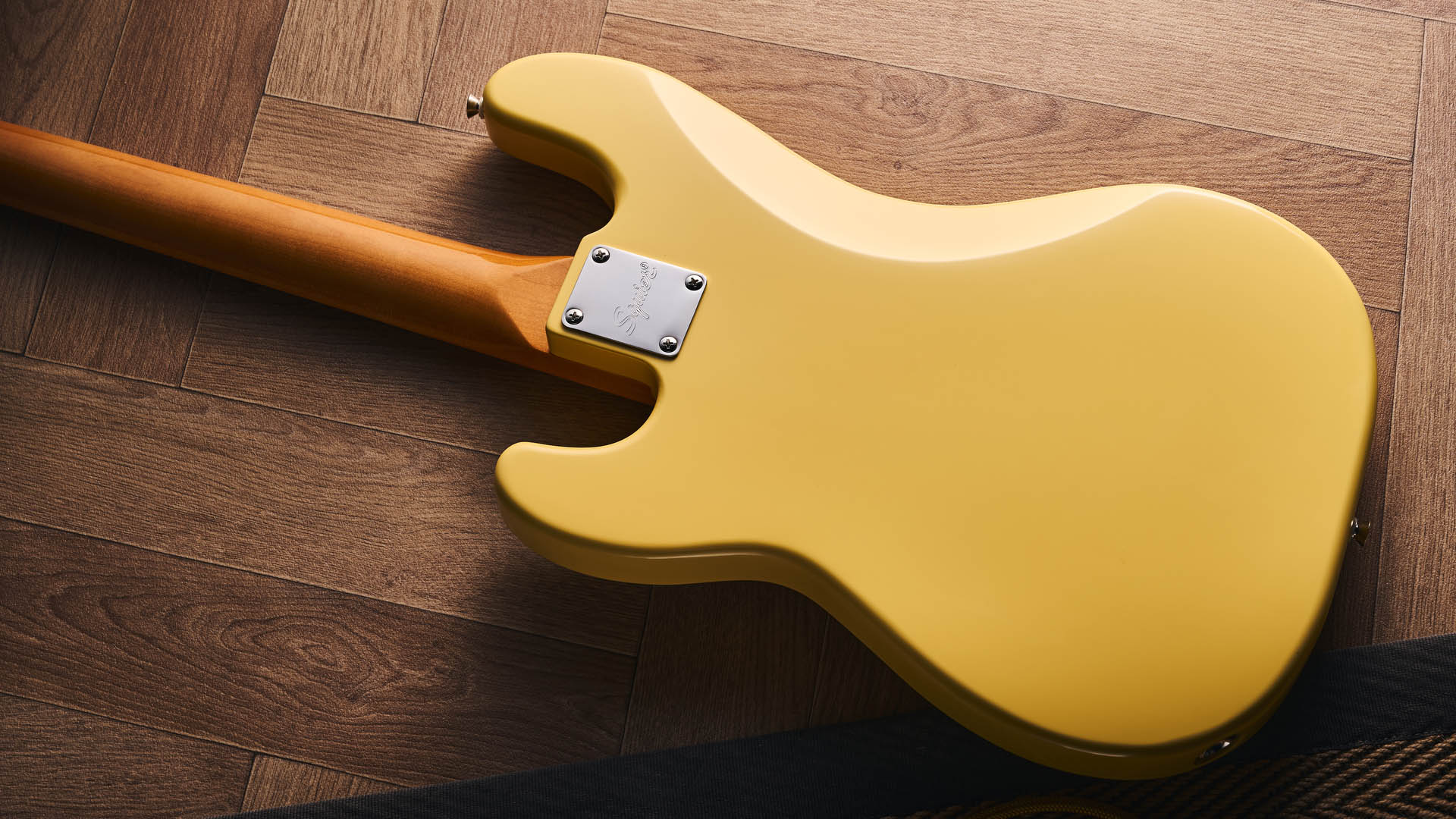 The Squier Classic Vibe Telecaster Bass is a fine-looking four-string in a custard-colored Vintage White, and is here photographed in close-up, against a plain wooden background. It has a single Wide Range humbucker.