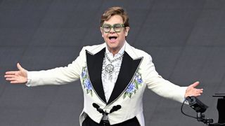 Elton John performs on stage wearing a bejewelled jacket and oversized green glasses ahead of Glastonbury 2023.