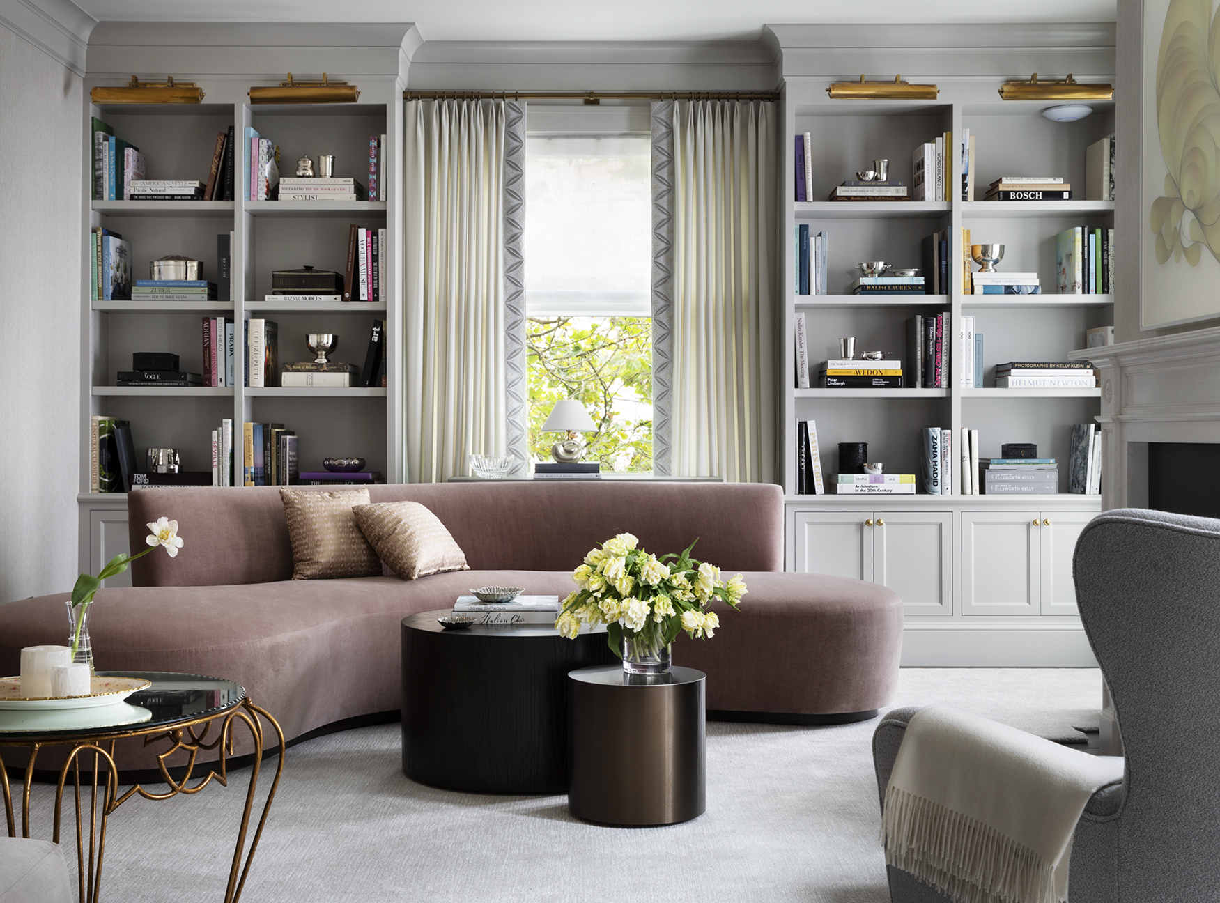 A curved peige sofa in a velvet fabric with silk cushions, in a contemporary library space