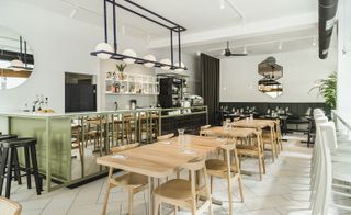 A long counter fronted with mirrors and glossy black tiles sits opposite a line of natural wood tables and chairs