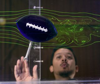 Student intern Joe Burces at NASA's Ames Research Center observes a football in fluid dynamics chamber.