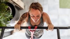 a shot from above of a woman performing a pull-up. there's a plant to the side of her and tiled floor beneath her.
