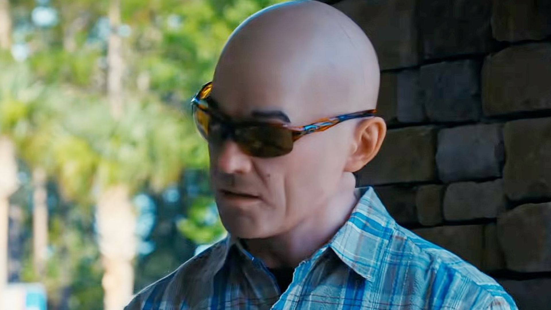 A masked bald man stand on a porch