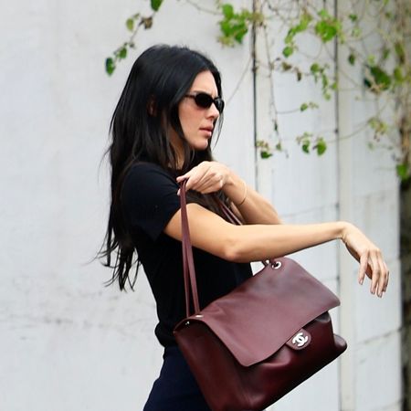 Kendall Jenner wearing a black T-shirt, relaxed-fit white jeans, burgundy ballet flats, and a burgundy Chanel Maxi Flapbag in Los Angeles