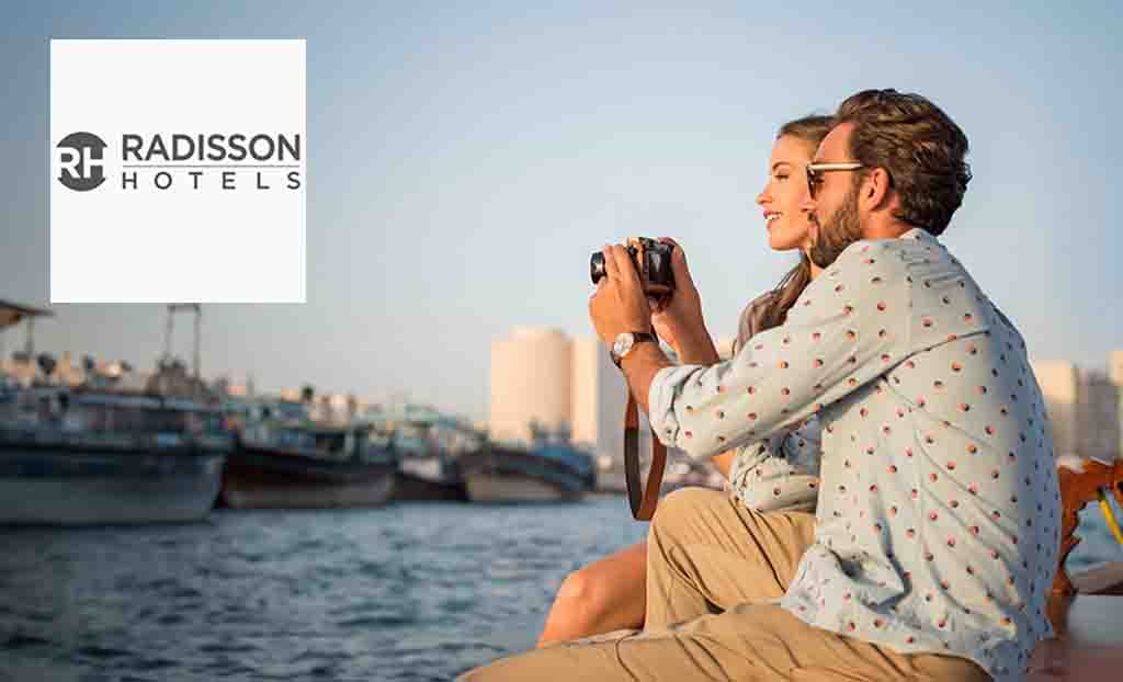 Radisson Hotels logo placed over an image of a couple taking a photo from across the river 