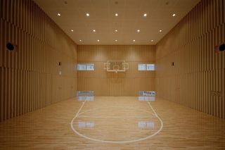 Indoor basketball court in light natural tones, illuminated by spotlights.