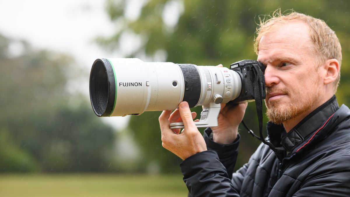 TechRadar Cameras Editor Tim Coleman holding the Fujifilm XF 400mm F4.5 R LM OIS WR telephoto prime lens attached to a Fujifilm X-H2S camera, out in the rain taking pictures