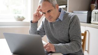 middle aged man sitting and looking at laptop with slight confusion and frustration