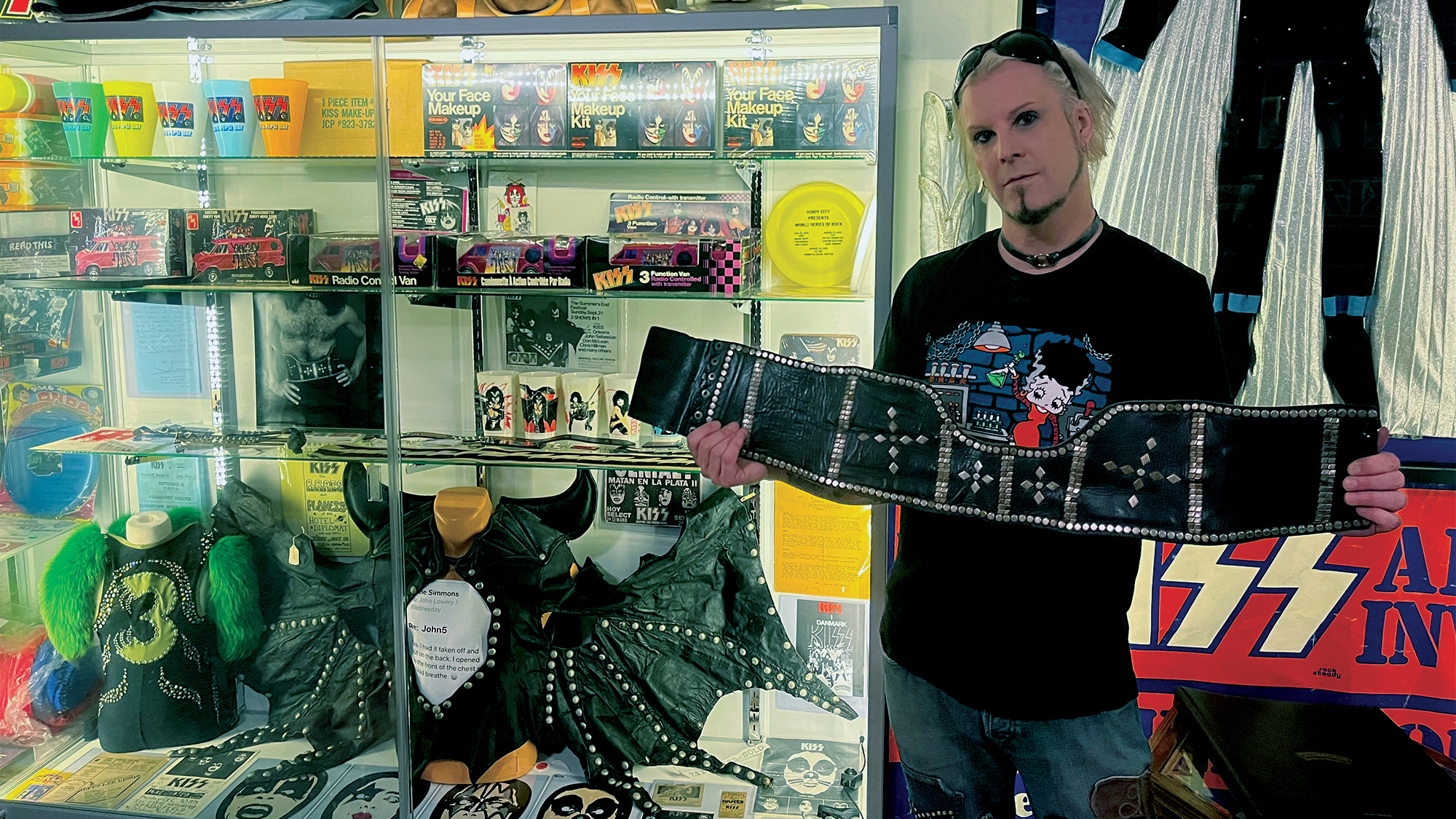 John 5 poses in his Knights in Satan's Service Museum of Kiss Memorabilia. John holds Paul Stanley’s leather-and-studs costume belt, seen on the cover of 1974’s Hotter Than Hell and subsequent tours. Gene Simmons’ original 1974 costume is in the glass case to his left.