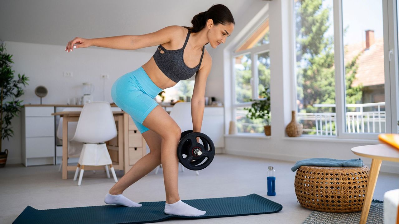 woman with dumbbell in hand does single-leg exercise at home 