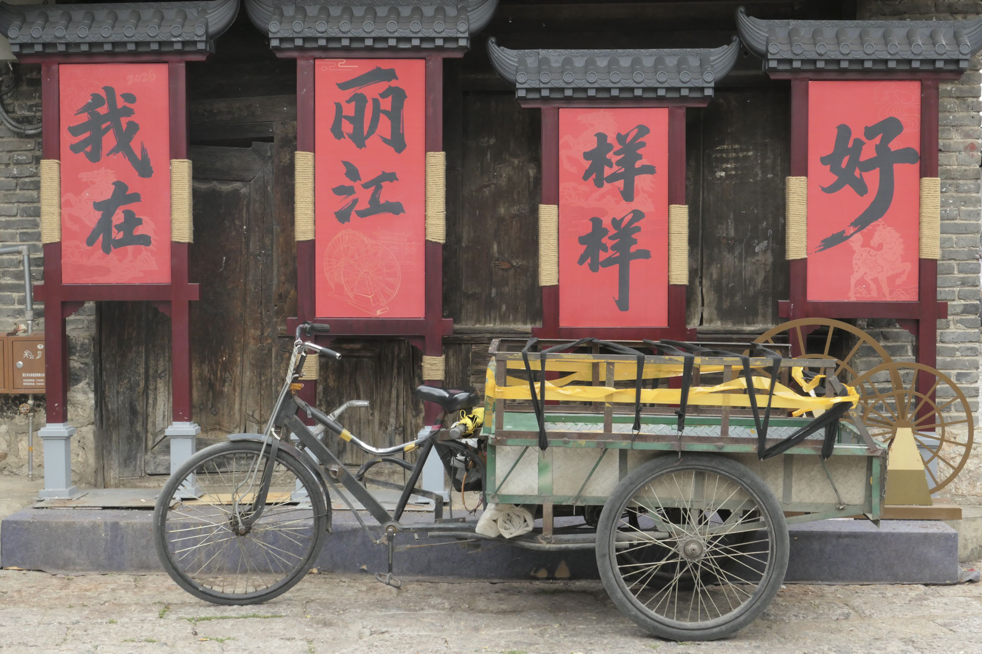 An old bike with a trailer, parked up in front of four Chinese posters
