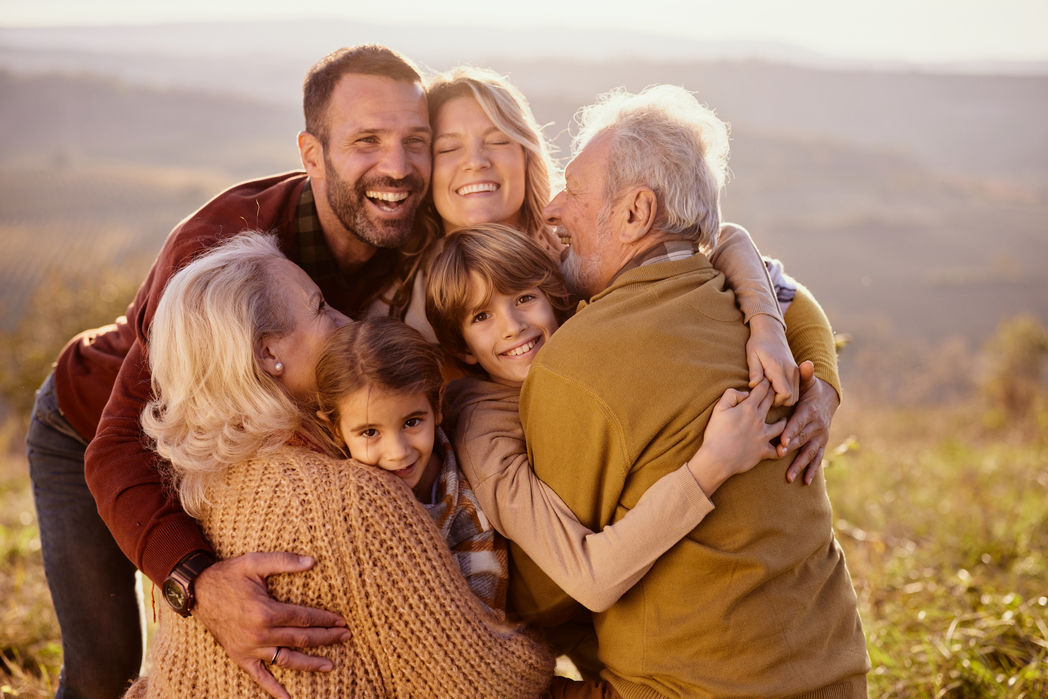 Happy multi-generation family embracing with great affection during autumn day on a hill.
