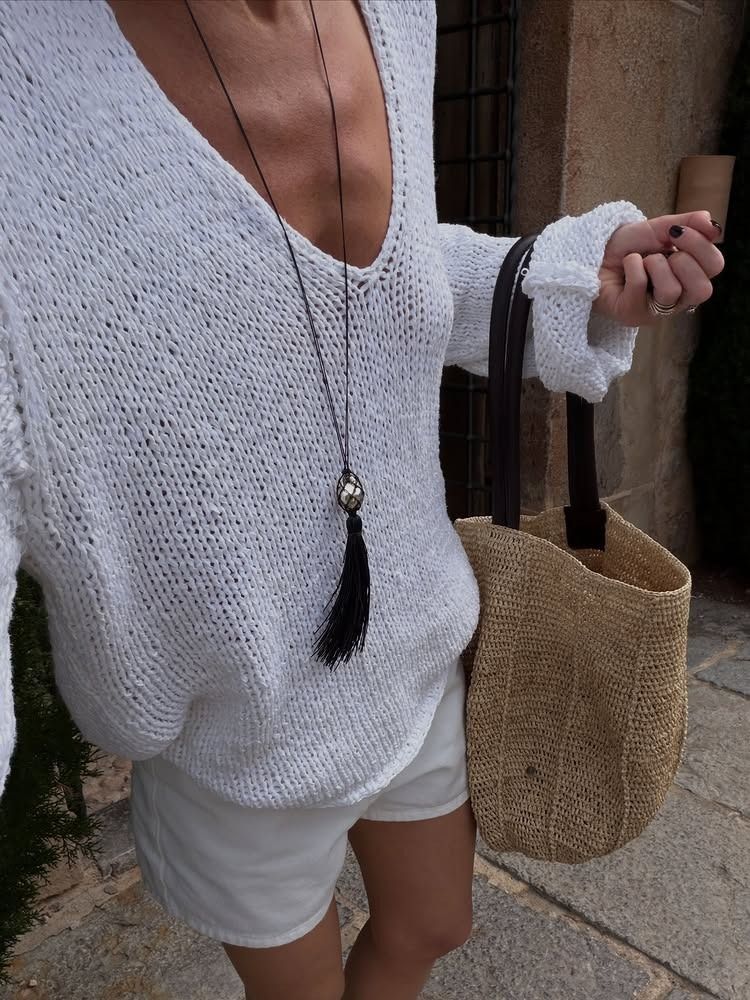 Hannah wears a white sweater, white shorts, and a raffia bag.