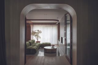 Looking through a curved archway into a living are with a green L-shaped sofa