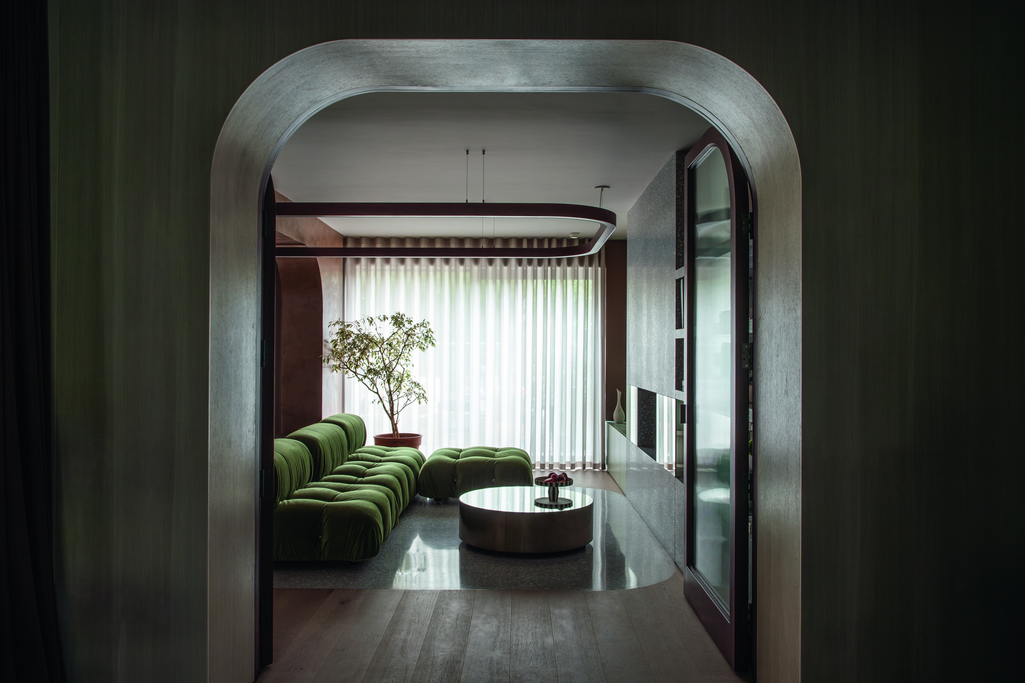 Looking through a curved archway into a living are with a green L-shaped sofa