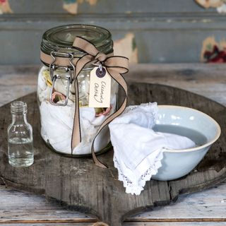 Bowl of white vinegar with a cloth in it, next to a mason jar full of cleaning cloths