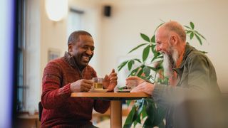 Two senior men are relaxing in a modern cafe, laughing and talking while enjoying green tea.
