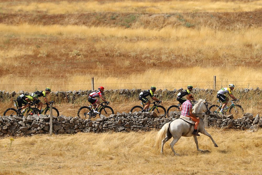 A rider on horseback runs with the Vuelta peloton during stage 10