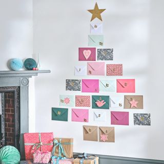 A wall Christmas tree made out of numbered envelopes and a gold star on top with wrapped presents on the floor