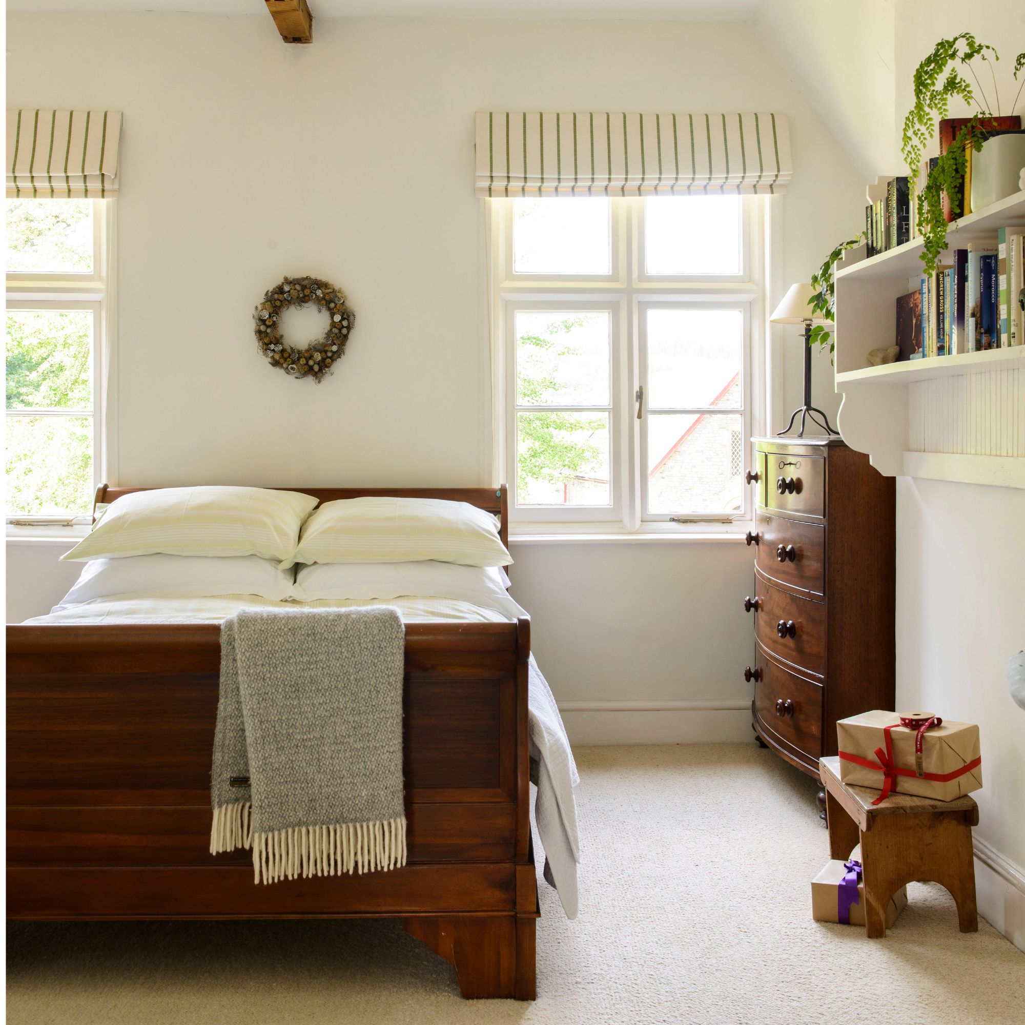 White painted bedroom with a dark wooden sleigh bed with white bedding, and a chest of drawers to the right