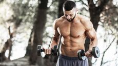 Man holding two dumbbells during workout standing outdoors in nature