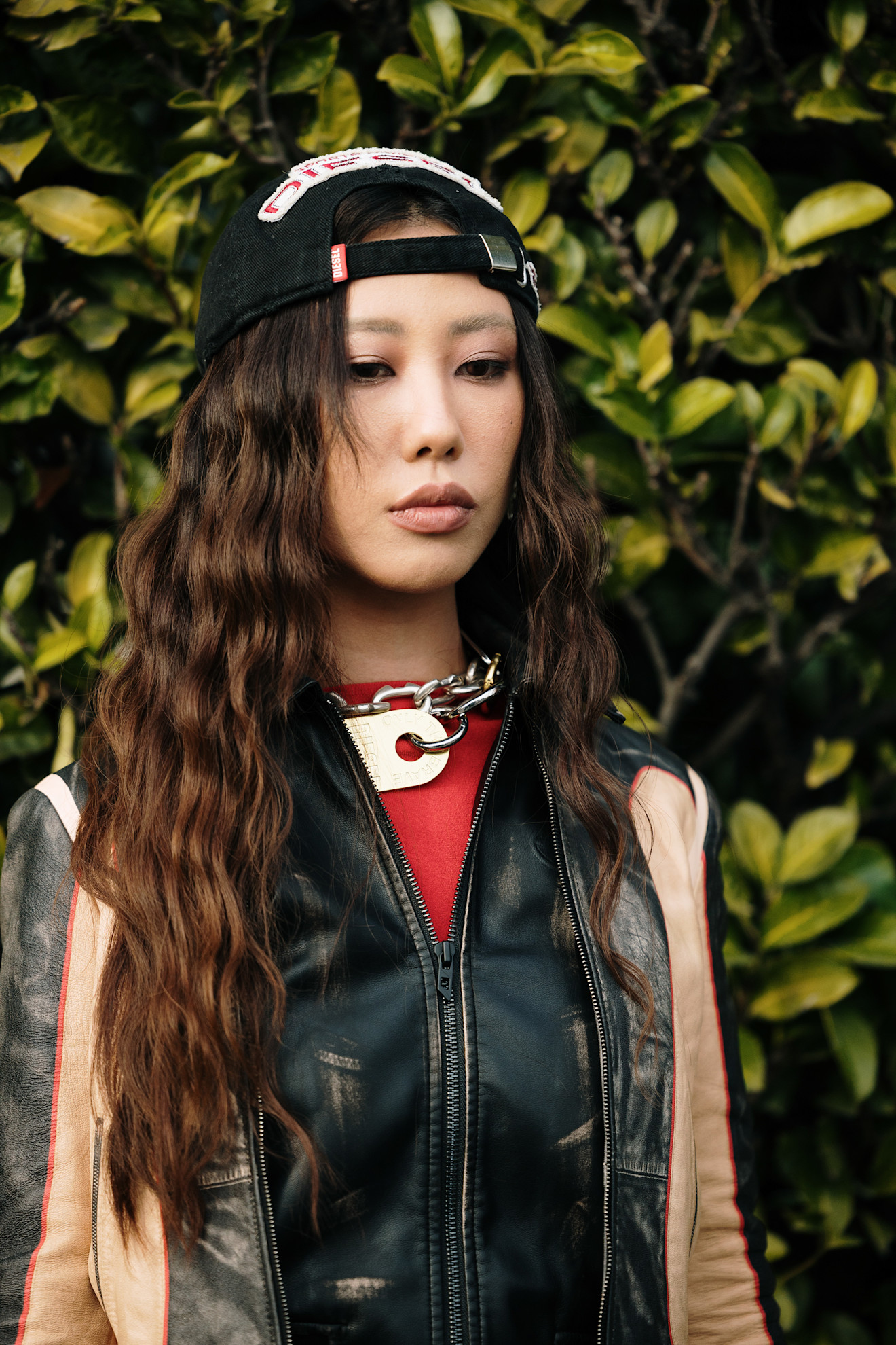 a woman with brown wavy hair in a backwards cap and leather jacket