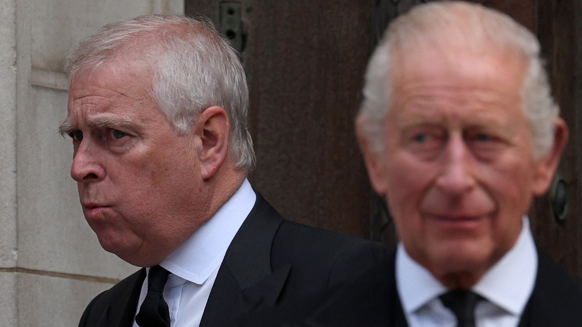 The former Prince Andrew wears a black suit with a white tie and has white gray hair and appears to be pursing his lips