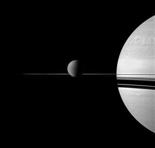 This image taken by the Cassini spacecraft highlights the thinness of Saturn's rings, only about one kilometer thick. Saturn's moon Titan looms over the thin rings, while the smaller moon Enceladus appears very tiny on the far right.