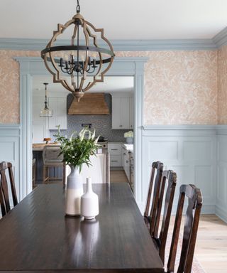 Modern heritage dining room with walnut dining table and chairs, and pastel blue wall paneling contrasted with coral floral wallpaper.