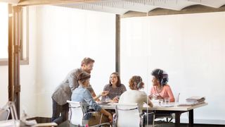 Office workers on a four-day week talking and laughing in a meeting room.