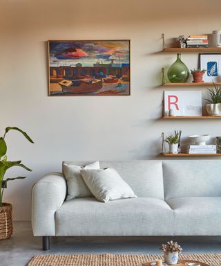 A small living room with a gray couch and a wall with wall art and shelving