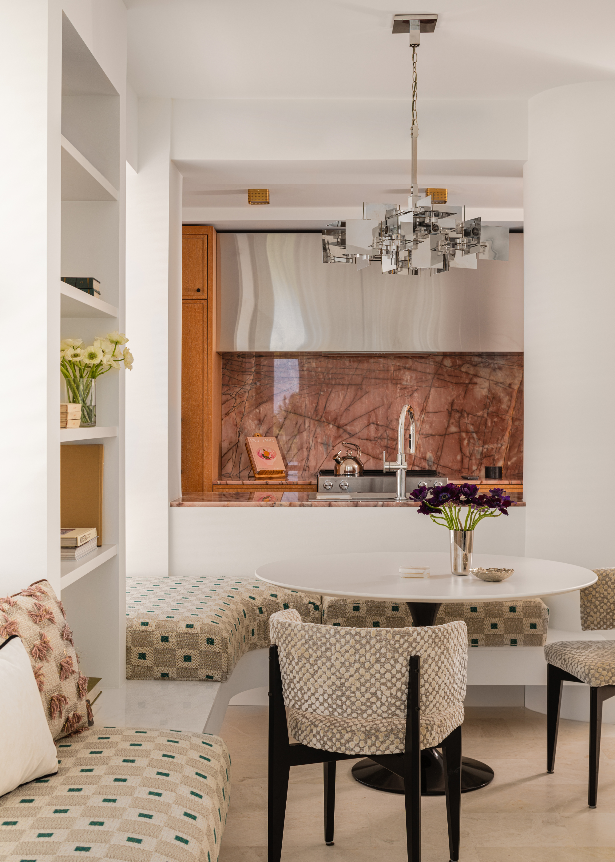 breakfast nook looking into a small kitchen with pink splashback and steel hood
