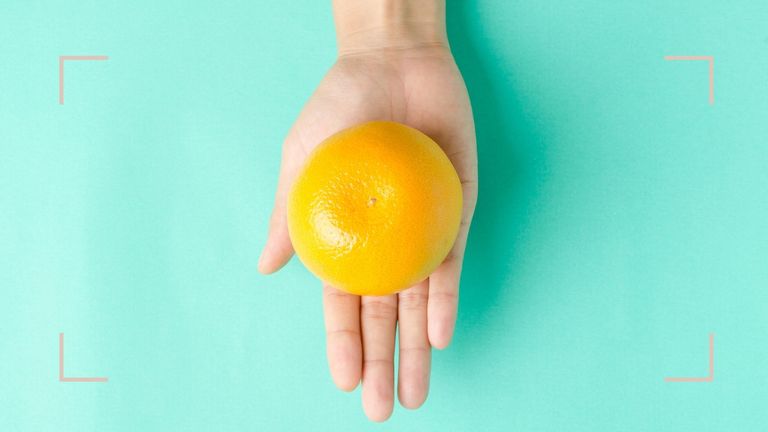 A woman's hand holding an orange to illustrate orange palms for how to get fake tan off hands