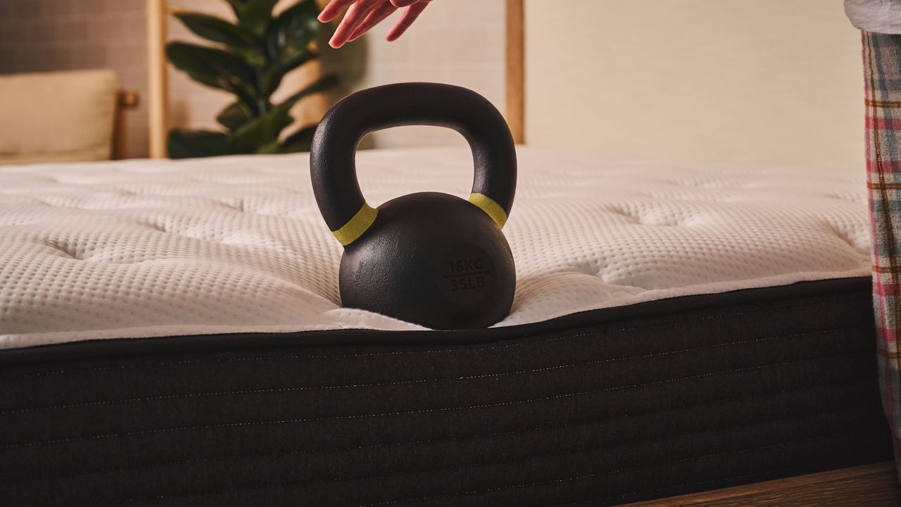A kettlebell balances on the side of the Plank Firm mattress, Firm side, testing the edge support